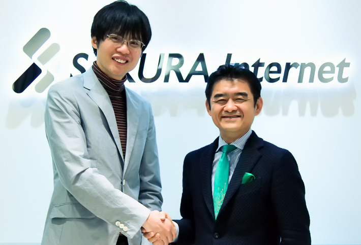 田中氏と平野、さくらインターネット会社ロゴ前で握手